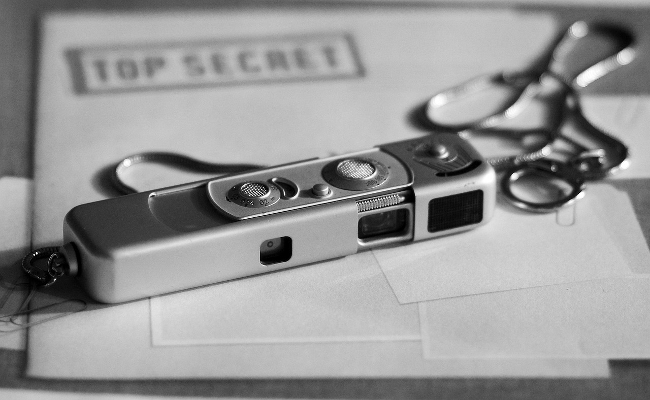 Vintage miniature spy camera resting on a folder labeled ‘Top Secret,’ with a chain attached.